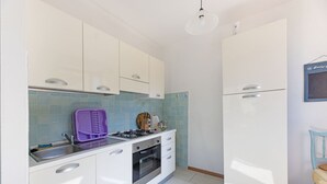 Una cocina compacta con armarios blancos, estufa a gas, horno empotrado y refrigerador blanco.