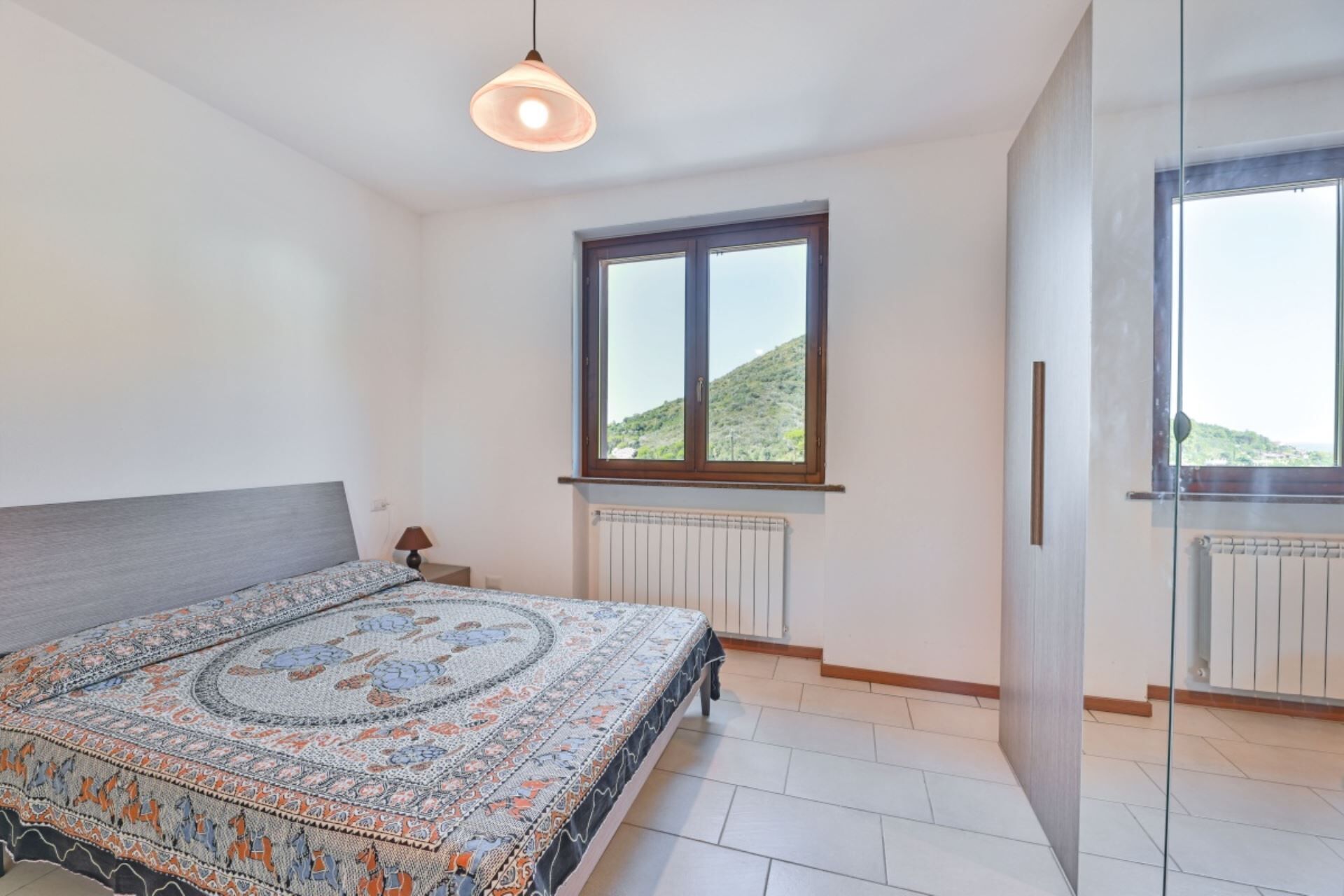 A bedroom with a bed, a window, a radiator, and a view of a hill.