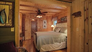 A wooden cabin interior with a bed, a ceiling fan, and a sign on the wall. - Black Bear Lodge Near Dupont State Forest (Hendersonville)