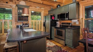 A wooden cabin interior with a kitchen featuring a refrigerator, microwave, stove, and a bar area with stools. - Black Bear Lodge Near Dupont State Forest (Hendersonville)