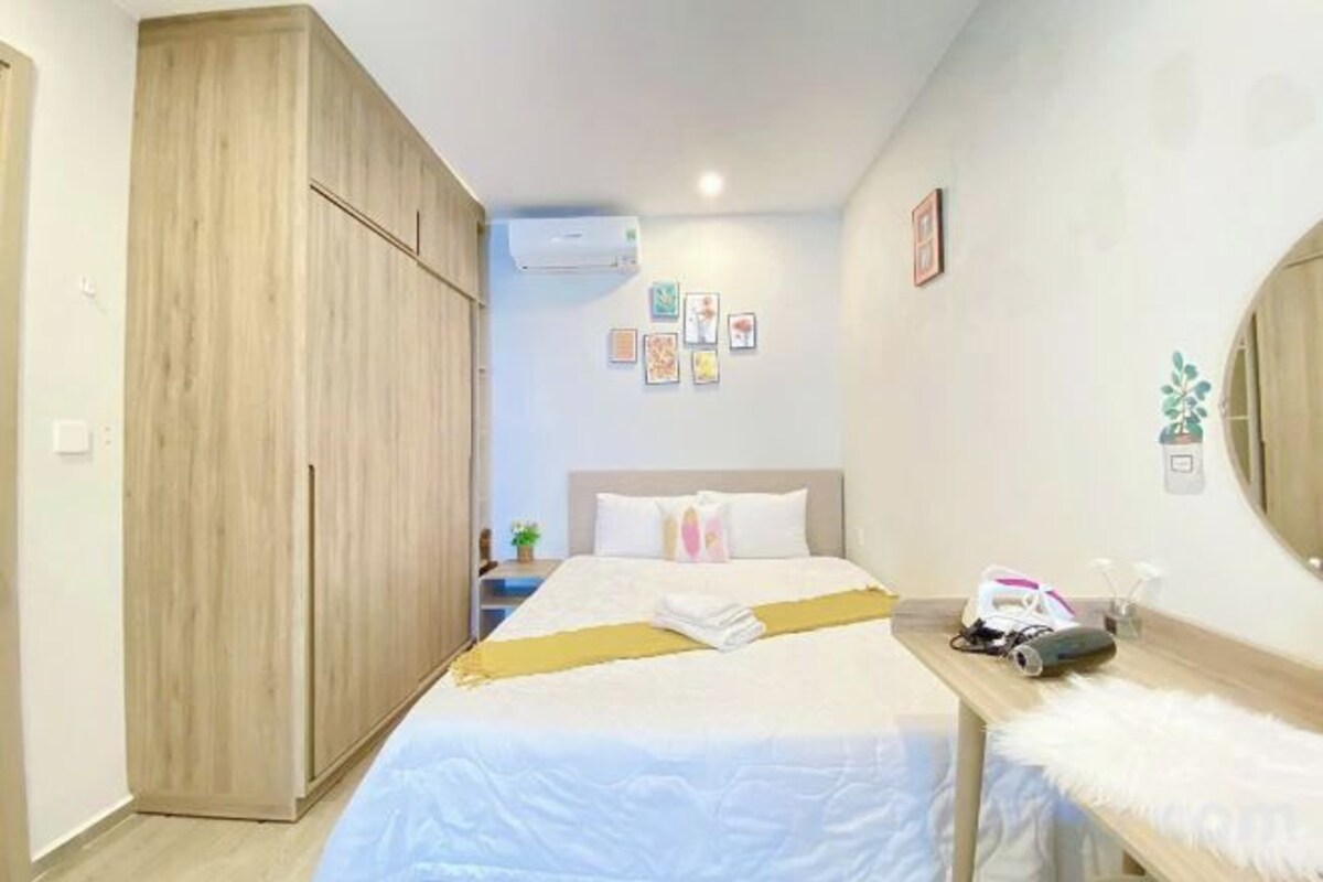 A bedroom with a bed, a wooden wardrobe, a bedside table, and a wall-mounted air conditioner.