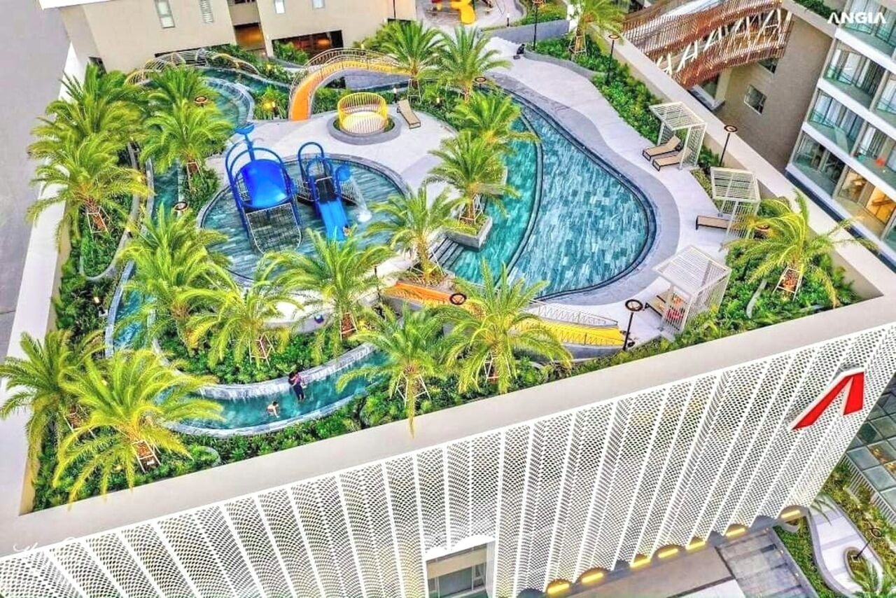 A rooftop pool area with a water slide, palm trees, and lounge chairs.