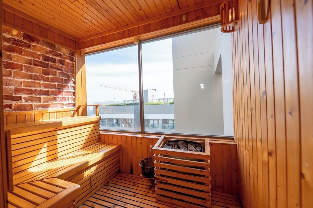 Una sauna amb bancs de fusta, una paret de maó i una finestra gran que ofereix vista a una zona de construcció.