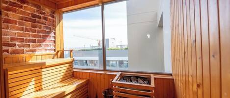 A sauna with wooden benches, a brick wall, and a large window offering a view of a construction site.