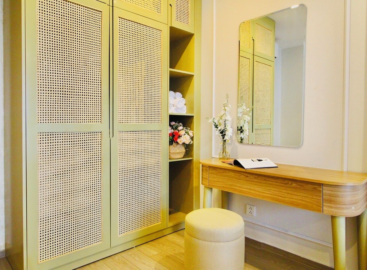 A room with a wooden vanity, a mirror, a wicker wardrobe, and a small stool.