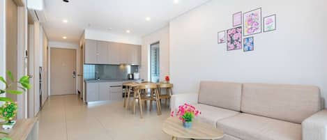A modern living room with a beige sofa, a wooden coffee table with a vase of flowers, and a dining area with wooden chairs and a table.