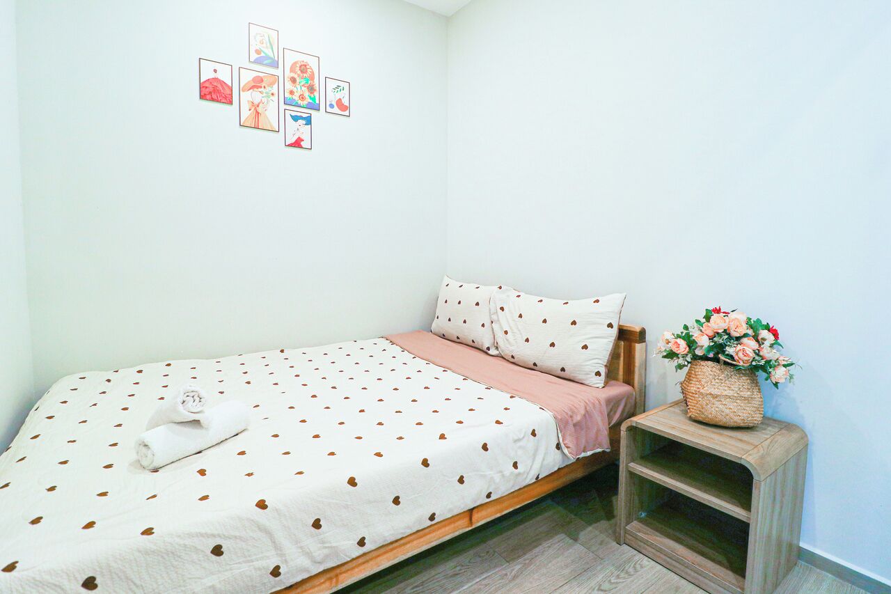 Un letto rifatto con cura, una coperta a pois, un asciugamano arrotolato e un comodino con un vaso di fiori.