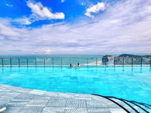Una piscina con agua azul cristalina, una barrera de vidrio y vistas a la playa y al horizonte de la ciudad.
