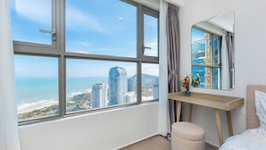 A modern bedroom with a large window, a bedside table, a mirror, and a view of the city and ocean. - The Song Vung Tau Apartment (Ho Chi Minh City)