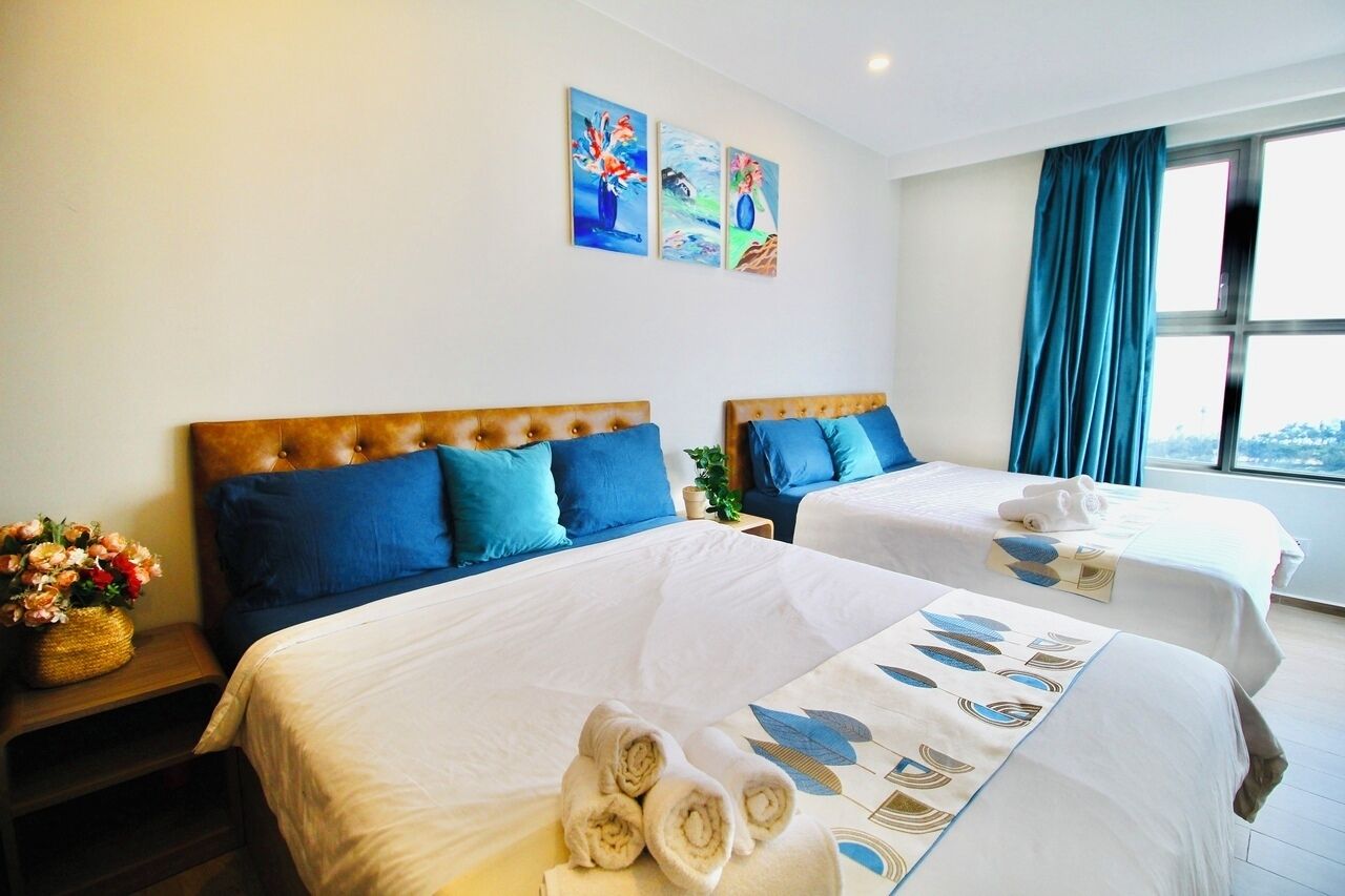 A hotel room with two beds, blue and white bedding, a window with curtains, and artwork on the wall.
