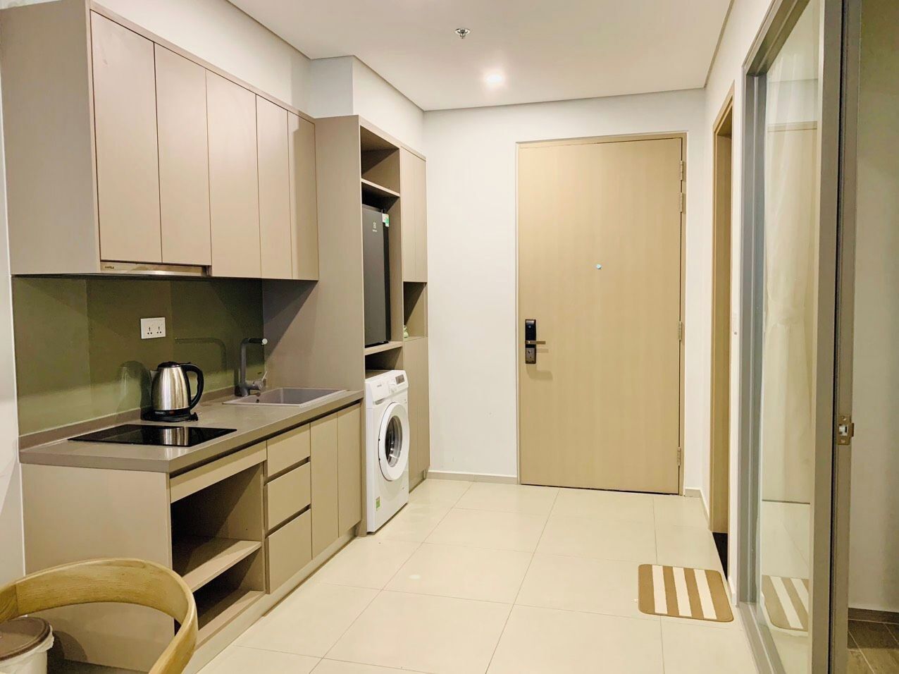 A compact kitchen with a washing machine, a kettle, and a sink.