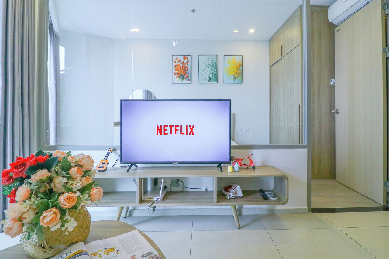 Una sala de estar moderna con un televisor de pantalla plana mostrando 'NETFLIX', un mueble de madera para entretenimiento y un jarrón con flores.