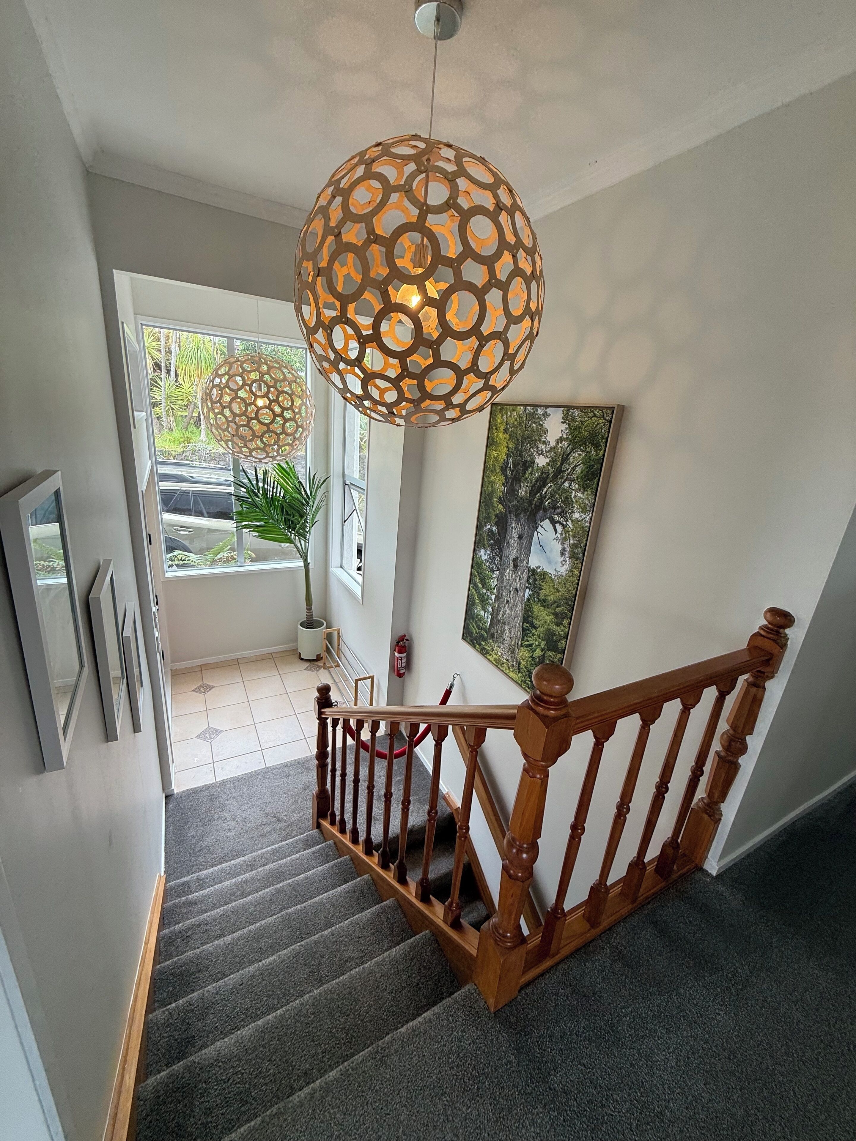 Un escalier avec une rampe en bois, un luminaire décoratif suspendu et un tableau encadré au mur.