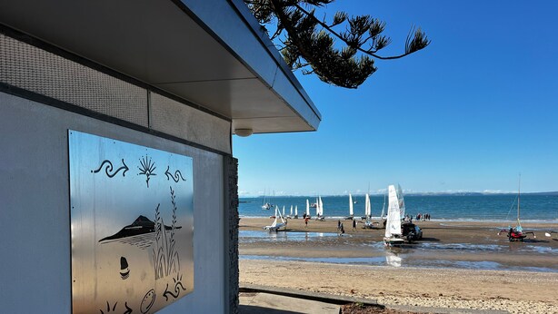 A beach with sailboats, a clear sky, and a building with a mural. - Waiake Beach Apartments (Auckland)