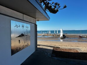 A beach with sailboats, a clear sky, and a building with a mural. - Waiake Beach Apartments (Auckland)