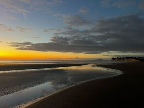 A beach with a calm sea, a clear sky, and distant mountains. - Waiake Beach Apartments (Auckland)