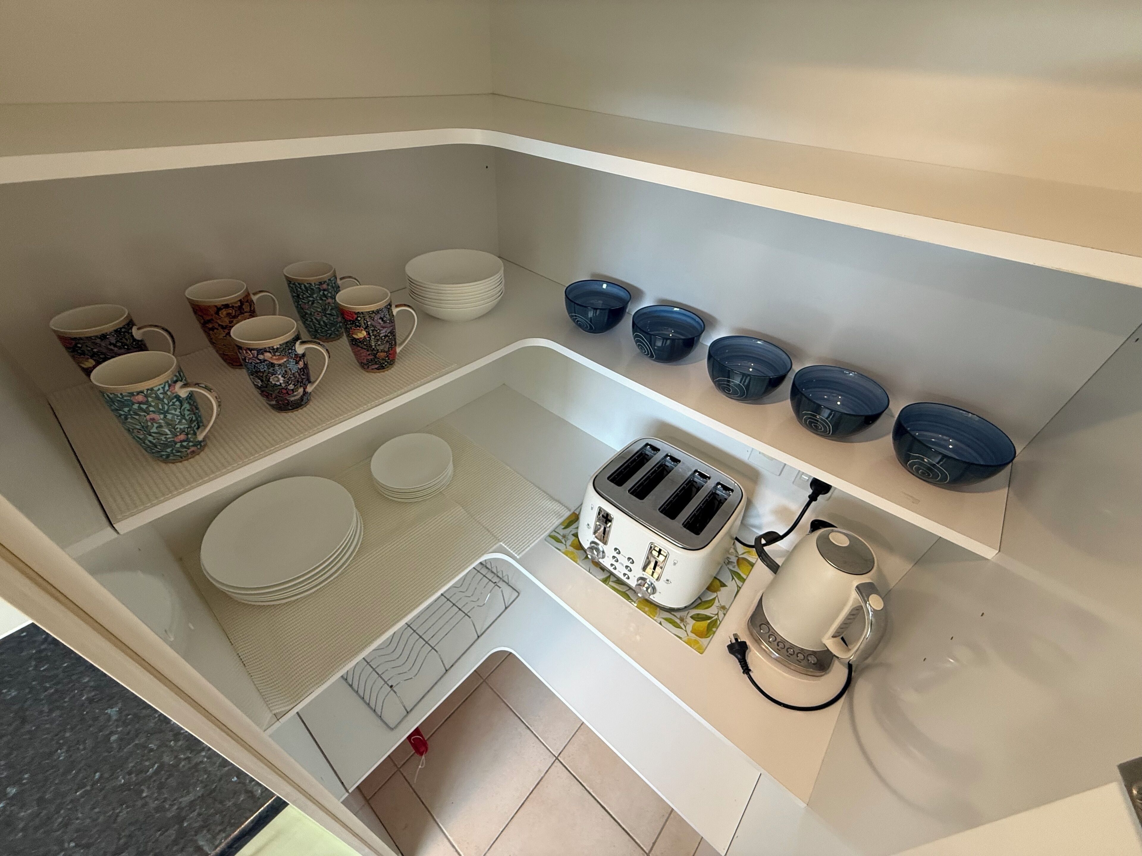 Eine kleine Küchenzeile mit Toaster, Wasserkocher sowie verschiedenen Tassen und Schüsseln.