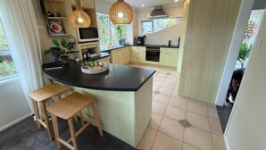 A modern kitchen with a central island, wooden cabinets, and pendant lighting. - Waiake Beach Apartments (Auckland)