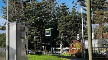 A park with a metal utility box, a sign indicating a walking path, and a metal fence.