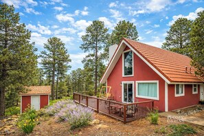 A red cabin with a balcony, surrounded by trees and a garden.