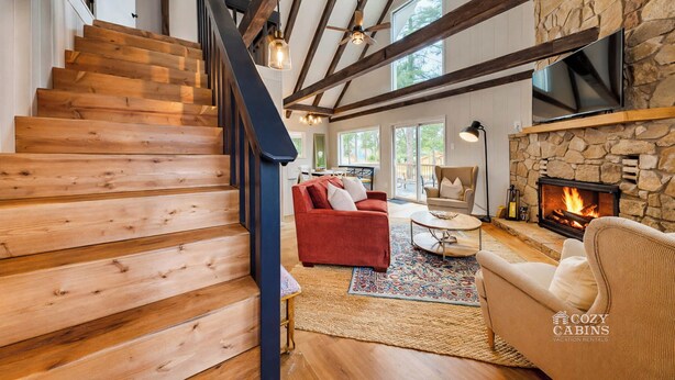Un escalier en bois mène à un espace de vie agrémenté d’une cheminée en pierre, d’un canapé rouge et d’un fauteuil beige.