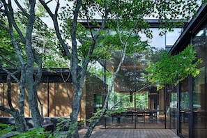 Un edificio moderno con grandes ventanales de vidrio, terraza de madera y árboles circundantes.