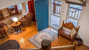 A wooden-floored living area with a blue door, a patterned rug, a sofa, a small table with a lamp, and a wooden bench. - Casa Bella 6 Bedrooms (Ruidoso)