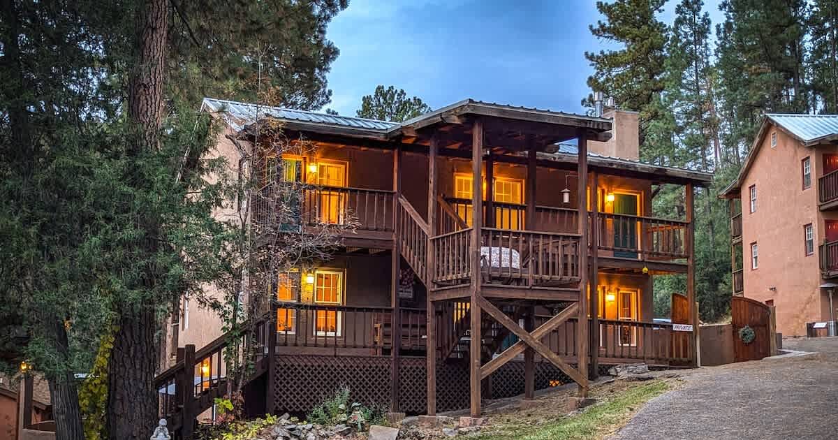Une cabane en bois à plusieurs étages, dotée d’un balcon et entourée d’arbres.