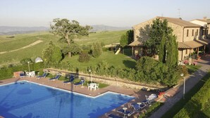 Ein Swimmingpool mit Liegestühlen, ein Steinhaus und eine grüne Landschaft mit Bäumen.