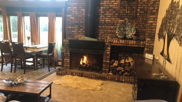 Un salon chaleureux avec une cheminée en briques, des meubles en cuir et un coin repas comprenant des chaises et une table.