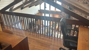 Un plancher en bois, un bureau, une chaise et un balcon donnant sur des meubles d’extérieur.