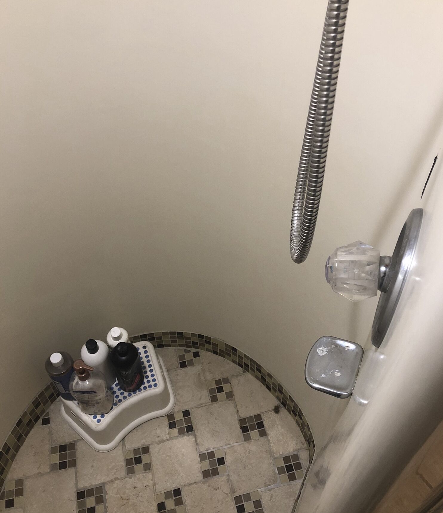 A small bathroom with a shower, a tiled floor, and a soap dish with bottles.