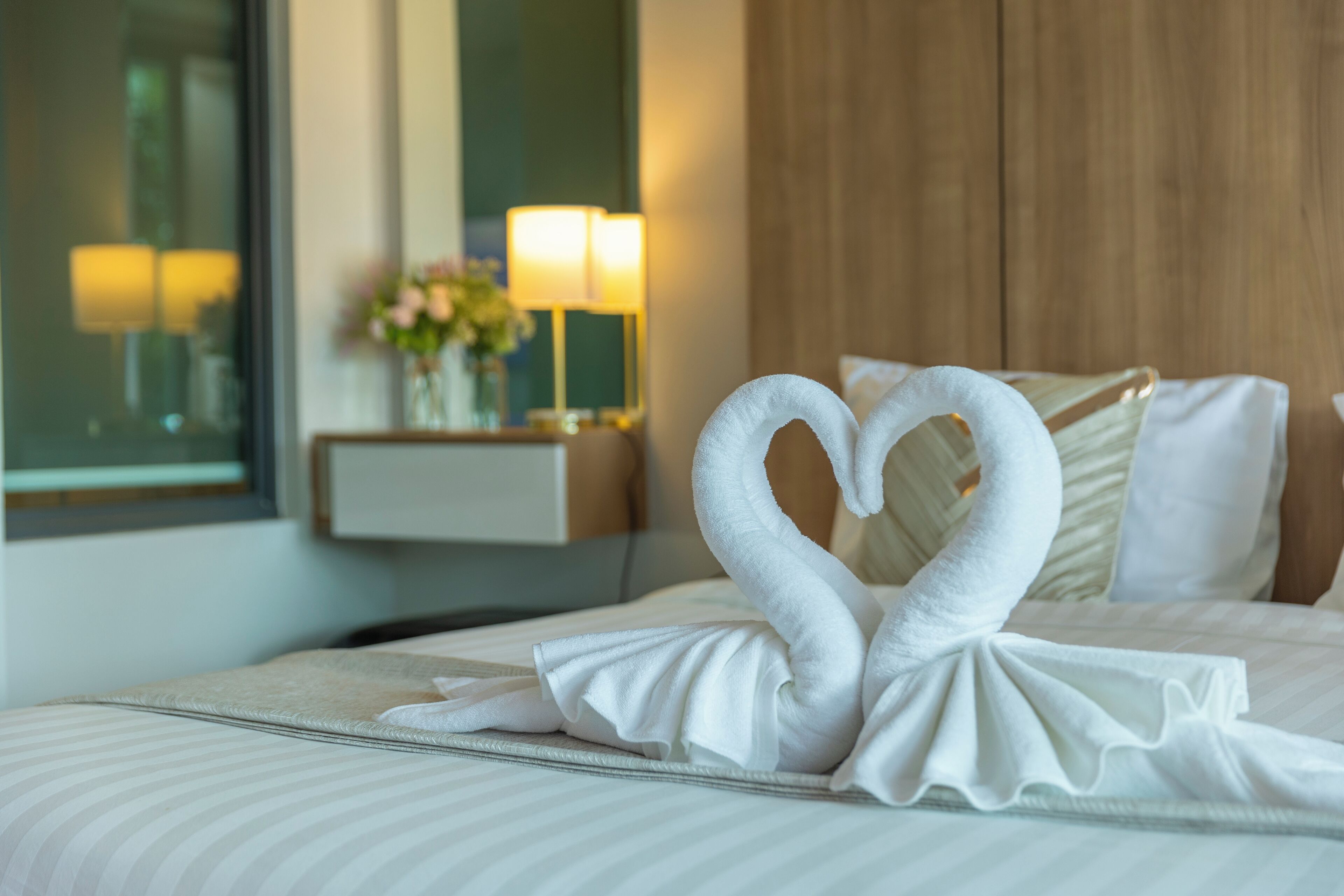 A hotel room with a neatly made bed, a bedside table with a lamp, and a mirror on the wall.