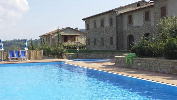 Una piscina con sillas de descanso y un edificio de piedra con balcón.