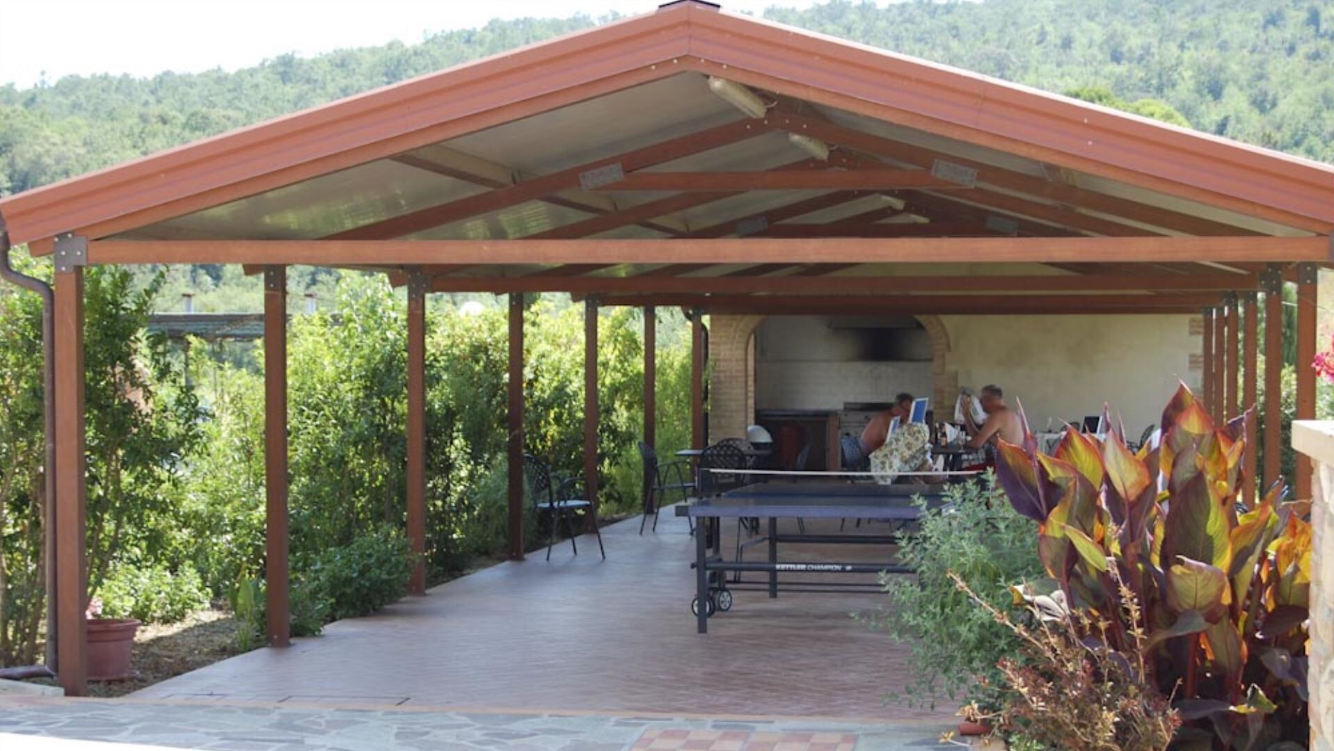A covered outdoor area with a barbecue setup, tables, and chairs.