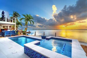 A swimming pool with a view of the sunset over water, a deck area with chairs, and a building with a balcony. - Into the Blues (Key West)