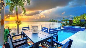 A poolside area with a table and chairs, a palm tree, and a view of the water.