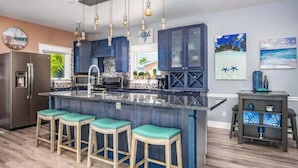 A modern kitchen with a central island, bar stools, and a refrigerator.