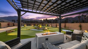 Un patio al aire libre con una chimenea, mobiliario de mimbre y un campo de golf al fondo.