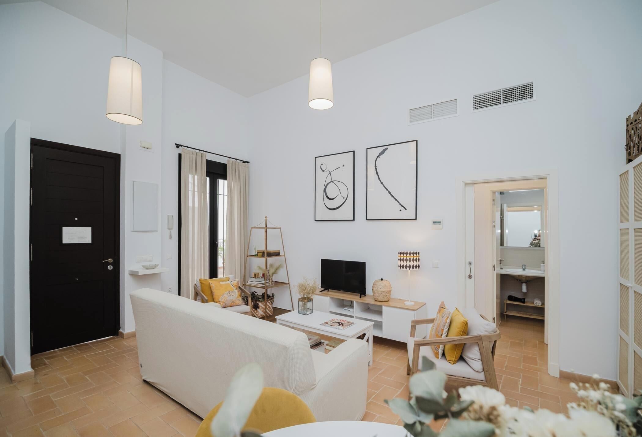 Una sala de estar con un sofá blanco, una mesa de centro, un televisor y obras de arte en la pared.