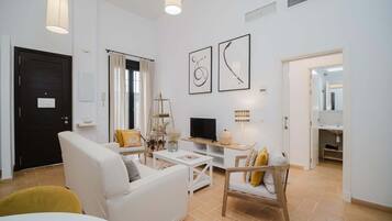 En moderne stue med sofa, sofabord, fjernsyn og kunst på væggen.