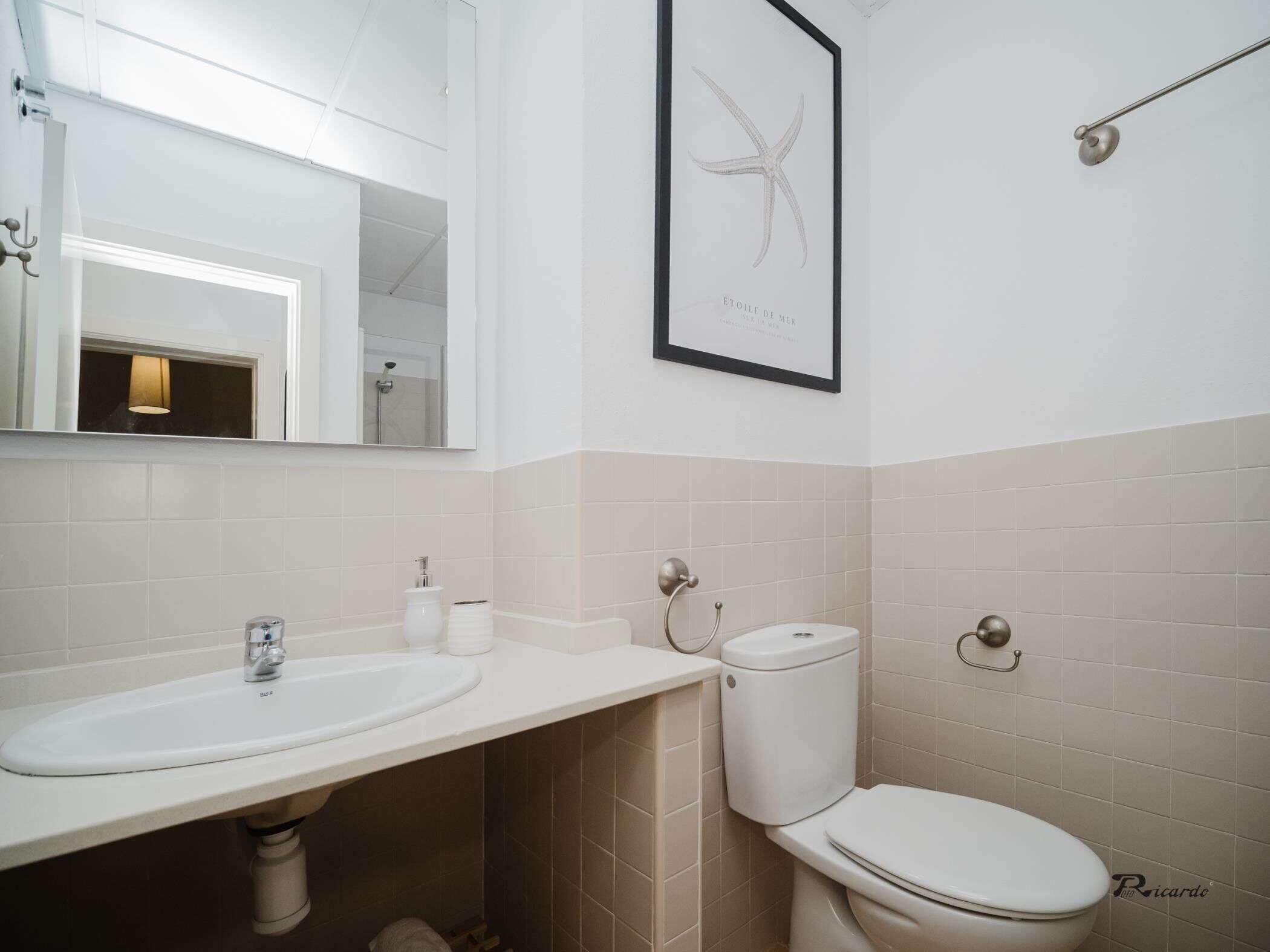 Een badkamer met een wit wastafel, toilet en een kunstwerk in een lijst aan de muur.