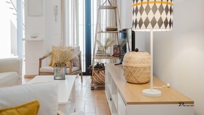 Een moderne woonkamer met een witte bank, een houten bijzettafeltje met een lamp en een boekenkast.