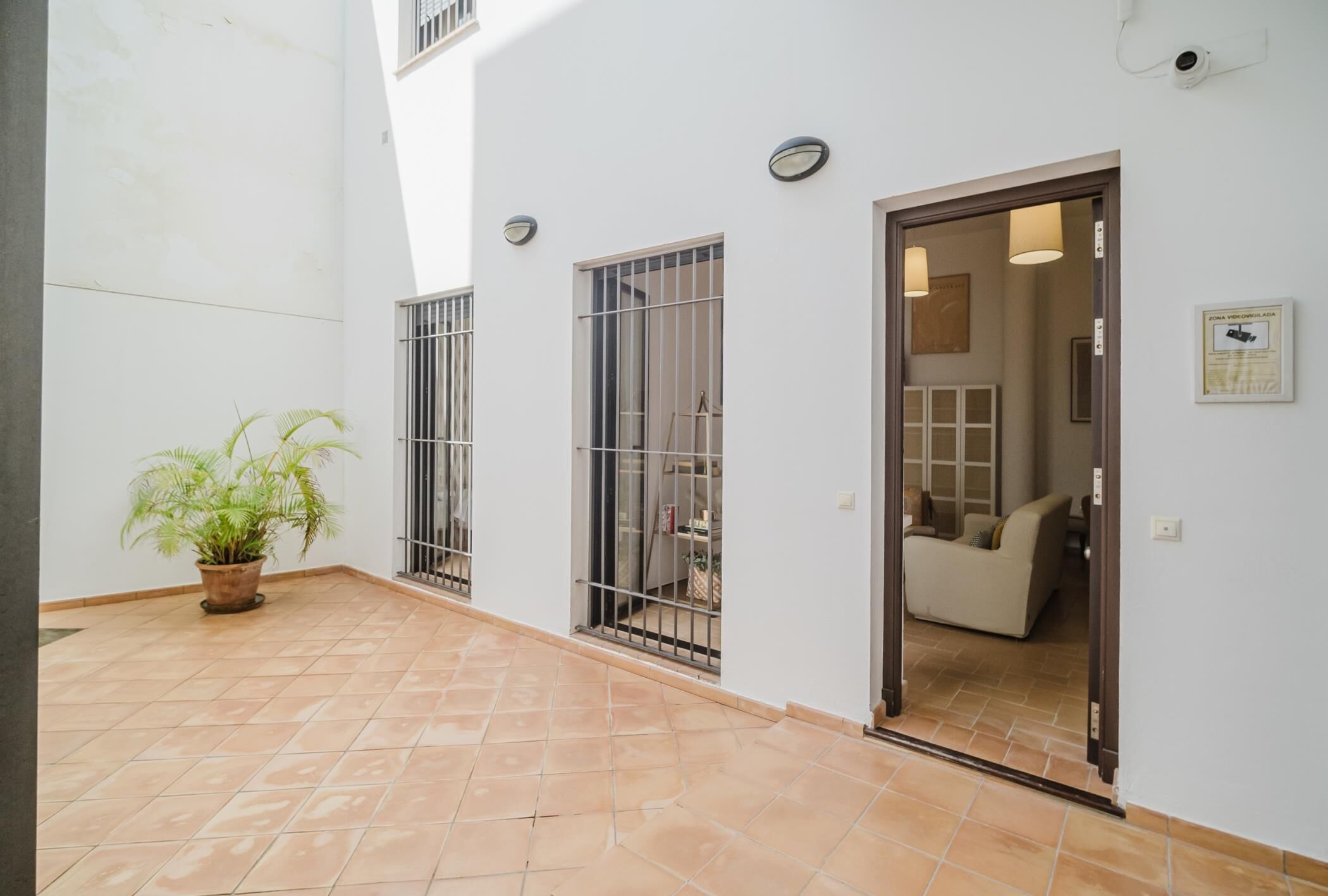 A spacious indoor area with a tiled floor, a potted plant, and a doorway leading to a room with a sofa.