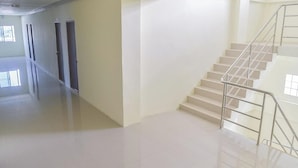 A spacious, well-lit hallway with a polished floor leading to a staircase with metal railings. - Orchid Residence At Amata (Phan Thong)