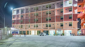 A multi-story hotel with a uniform facade, a parking lot, and a few people outside. - Orchid Residence At Amata (Phan Thong)