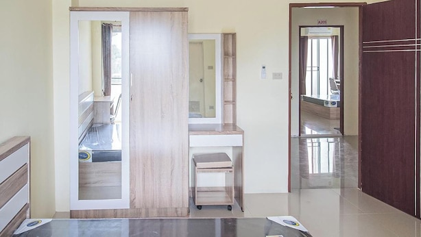 A room with a wooden wardrobe, a vanity with a mirror, and a small seating area. - Orchid Residence At Amata (Phan Thong)