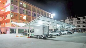 A parking area with a white delivery truck and several cars parked under a covered structure. - Orchid Residence At Amata (Phan Thong)