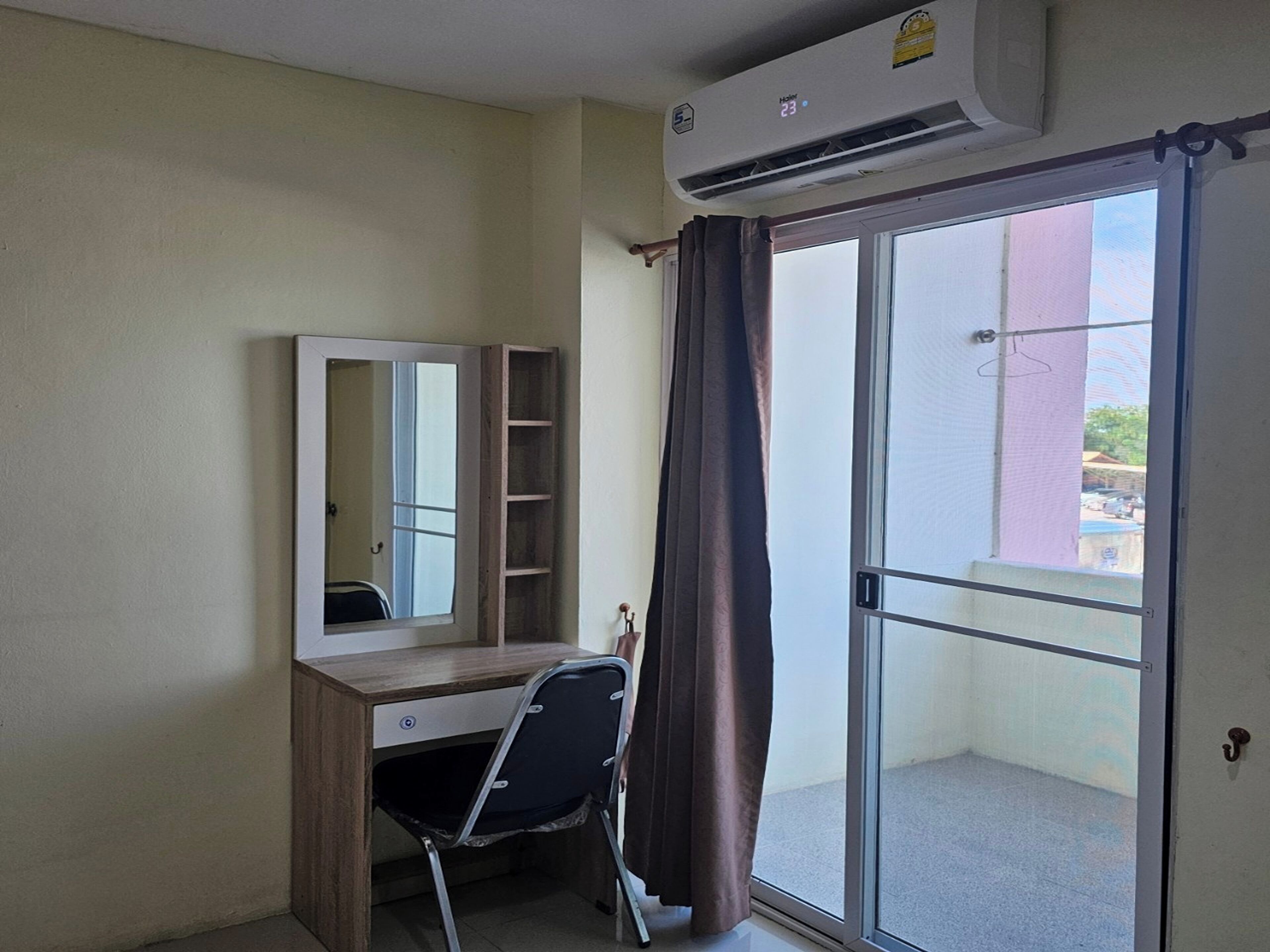 Habitación con escritorio, silla, espejo y puerta corrediza de vidrio a un balcón.