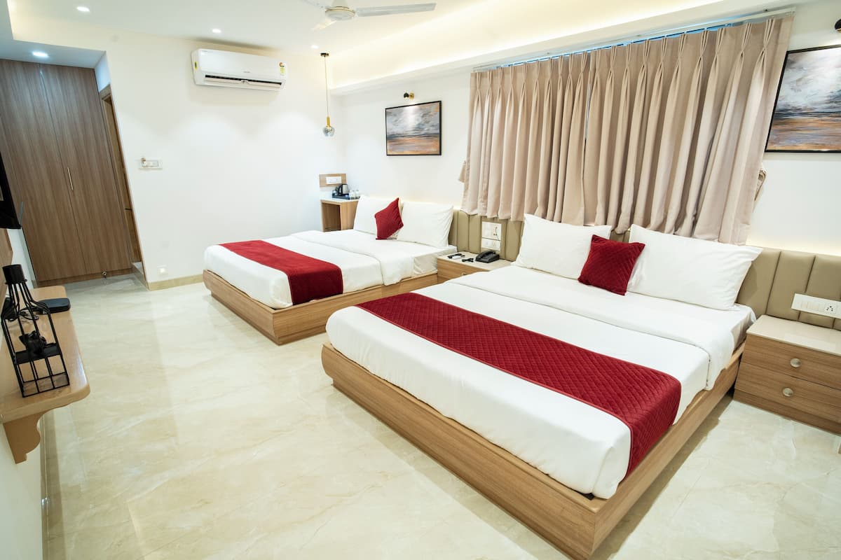 A hotel room with two beds, a desk, a wardrobe, and an air conditioning unit.